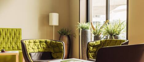 A modern room with green upholstered chairs, a wooden table, and potted plants.