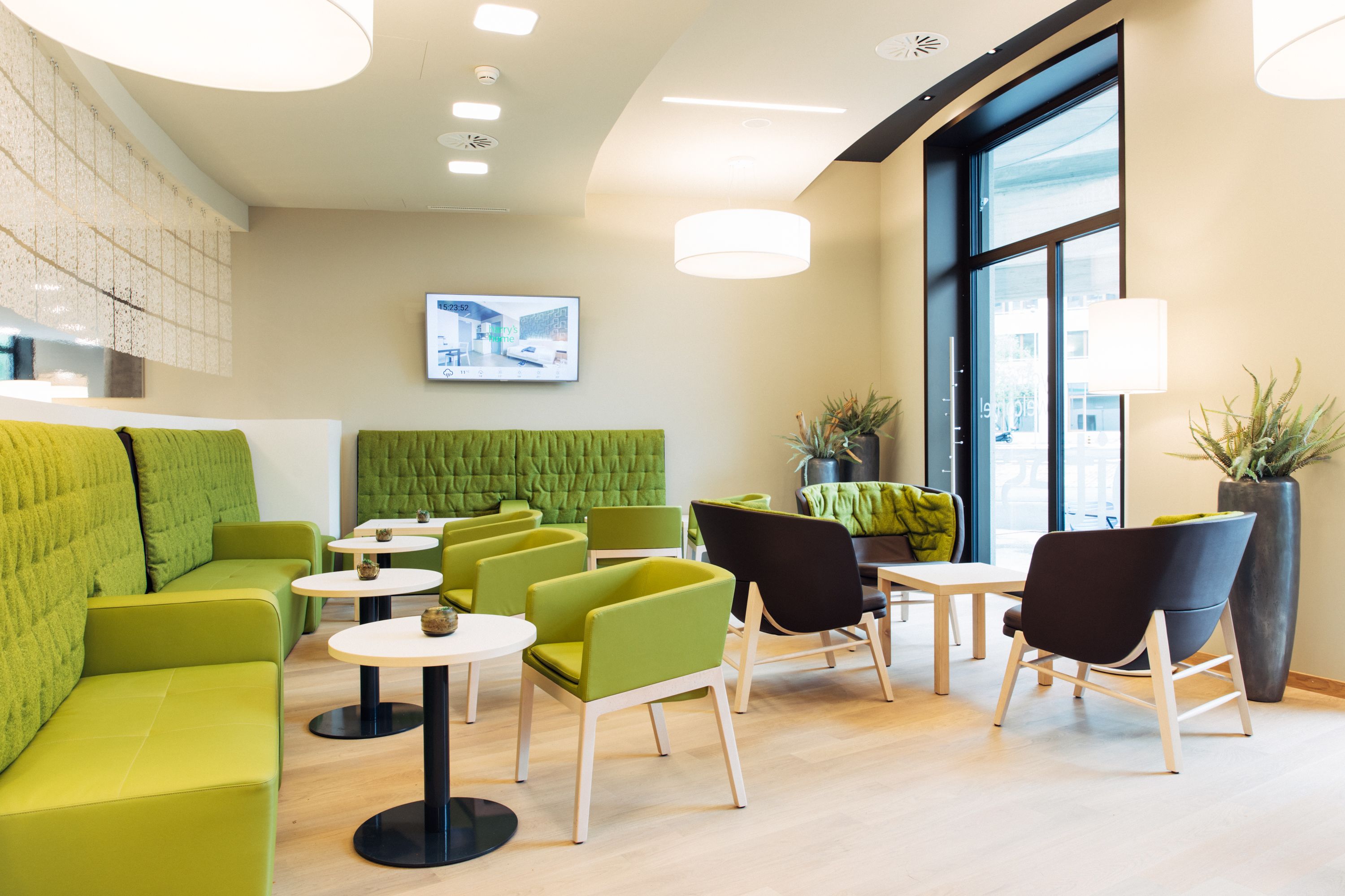 Ein moderner Lounge-Bereich mit grünen Sitzgelegenheiten, kleinen Tischen und großen Fenstern.