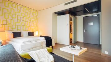Une chambre d’hôtel moderne avec un lit soigneusement fait, une petite table sur laquelle reposent une paire de lunettes de soleil et une armoire.