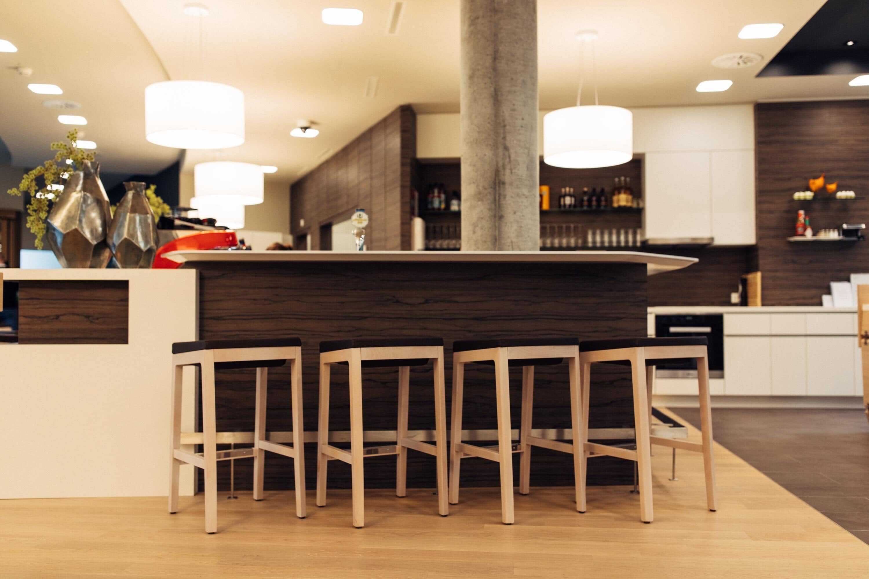 Un área de bar moderna con taburetes de madera, una columna central e iluminación colgante.