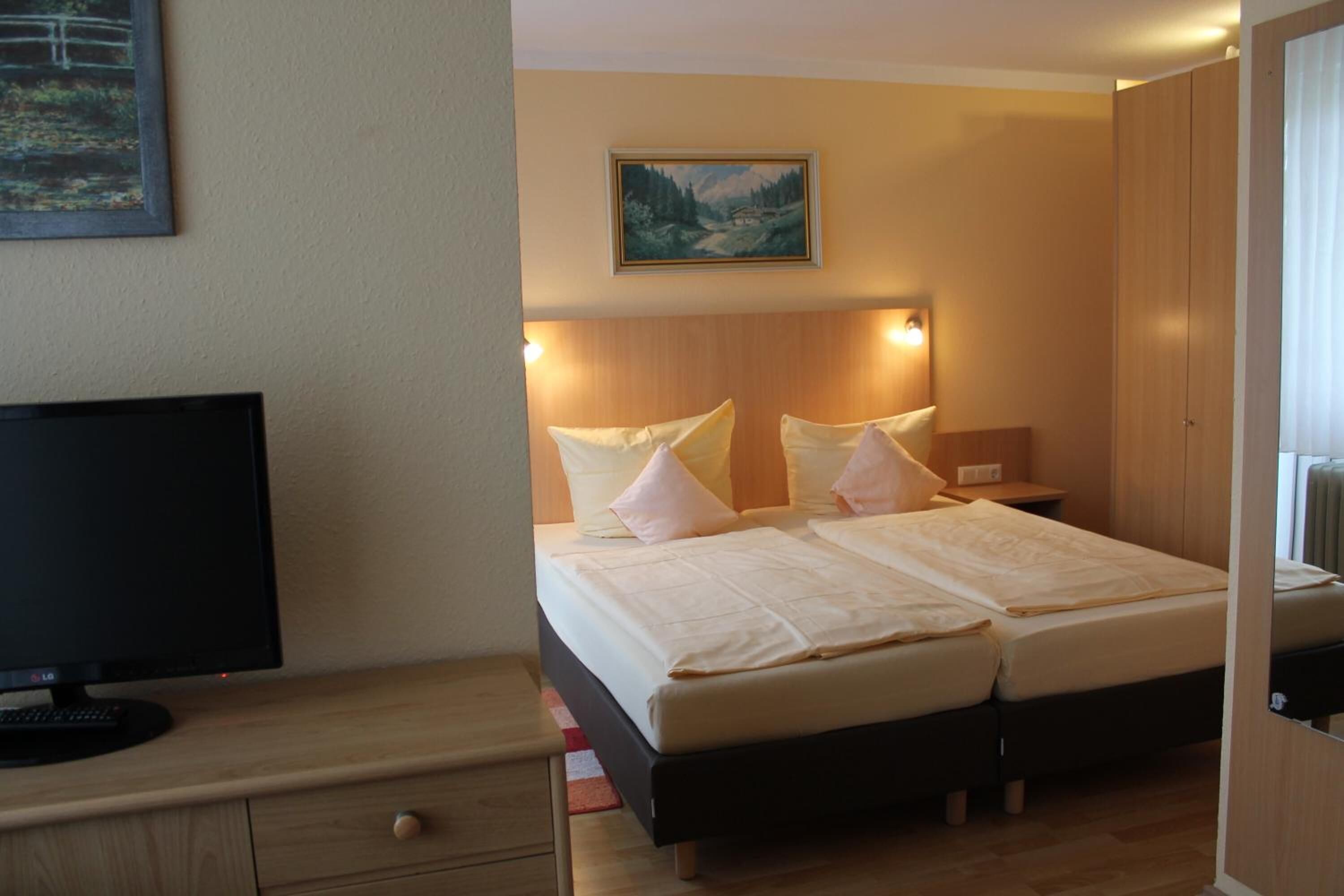 A hotel room with a bed, a TV, and a painting on the wall.