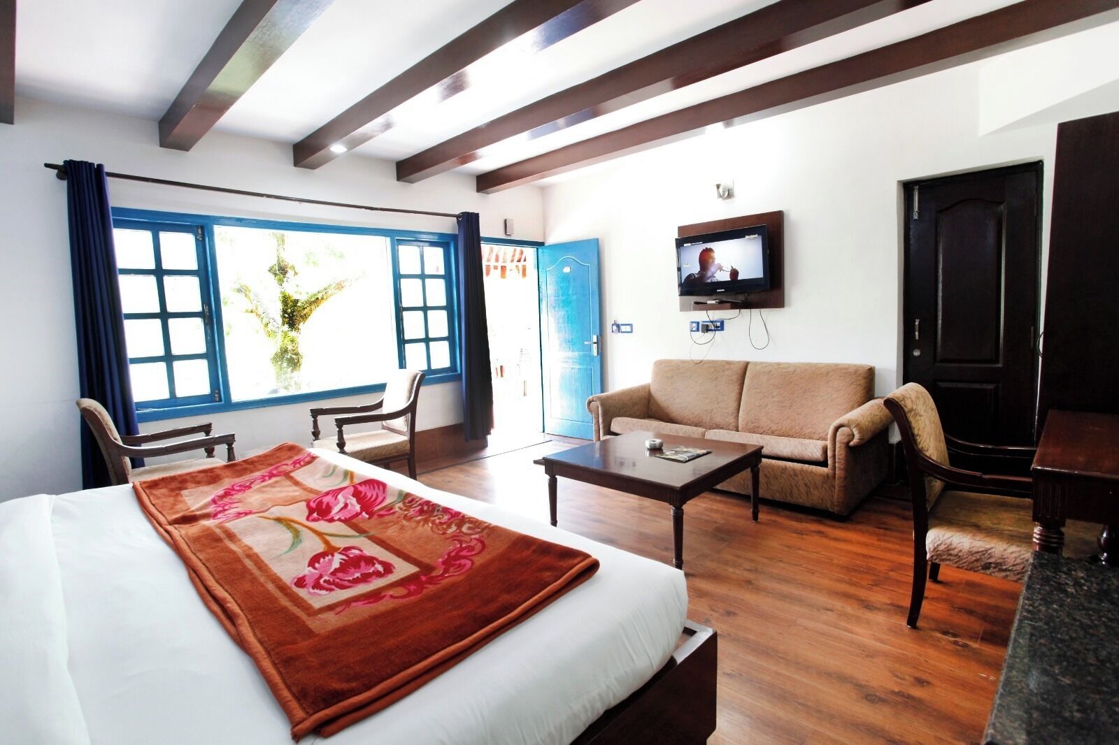 A hotel room with a bed, a sofa, a coffee table, a TV, and a window with curtains.