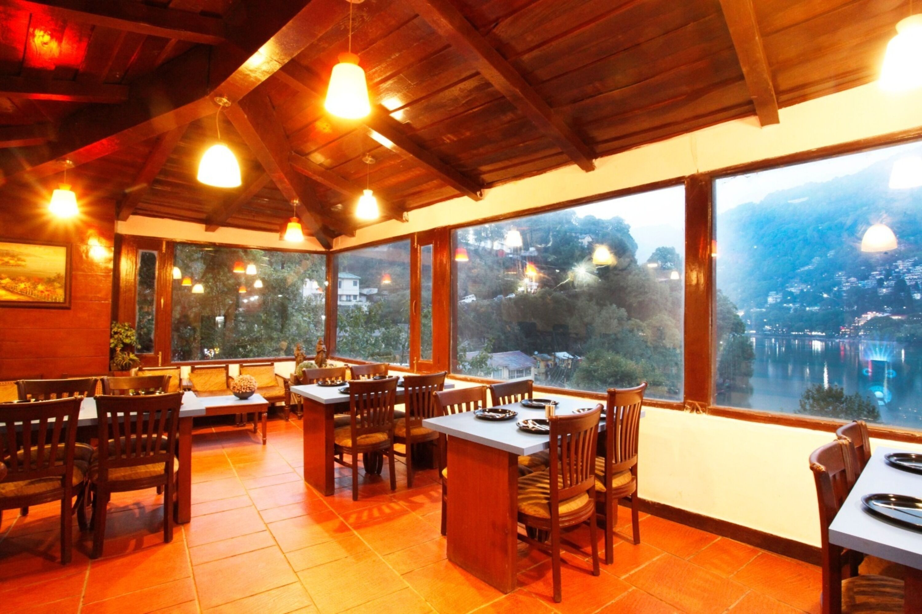 Un restaurante con muebles de madera y ventanas amplias que ofrecen vistas a un lago y colinas.