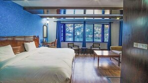 A bedroom with a large bed, a wooden headboard, a nightstand, a mirror, and a window with curtains. - Manu Maharani Regency (Nainital)