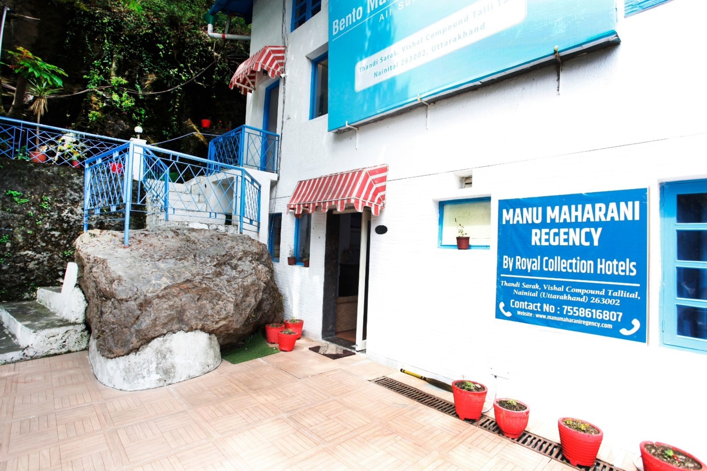A building with a sign for "Manu Maharani Regency by Royal Collection Hotels" and a large rock in front.
