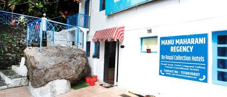 A building with a sign for "Manu Maharani Regency by Royal Collection Hotels" and a large rock in front.