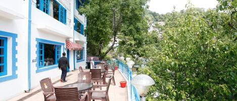 A terrace with outdoor seating, a person walking, and a view of greenery.