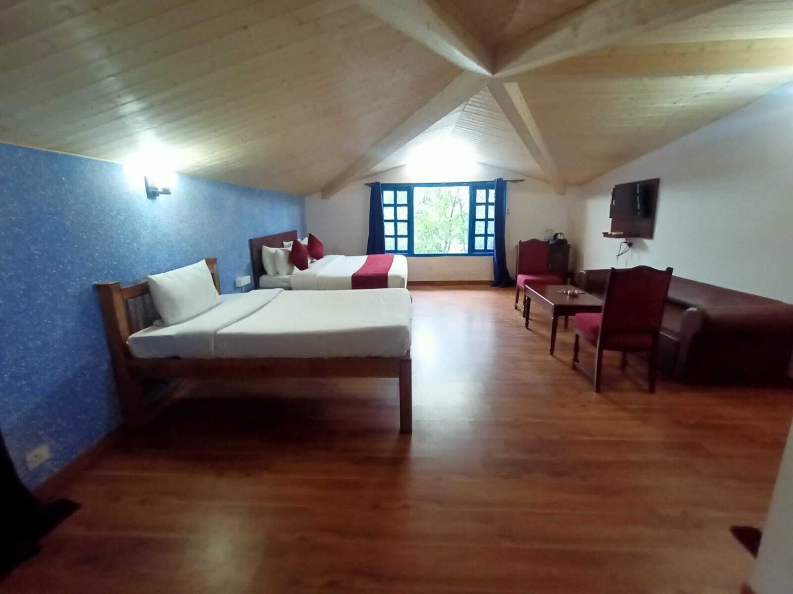 A room with two beds, a wooden ceiling, a TV, and a window with blue curtains.