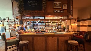 A bar area with a wooden counter, stools, and a variety of liquor bottles. A chalkboard sign is visible above the counter. - Great Malvern Hotel (Malvern)