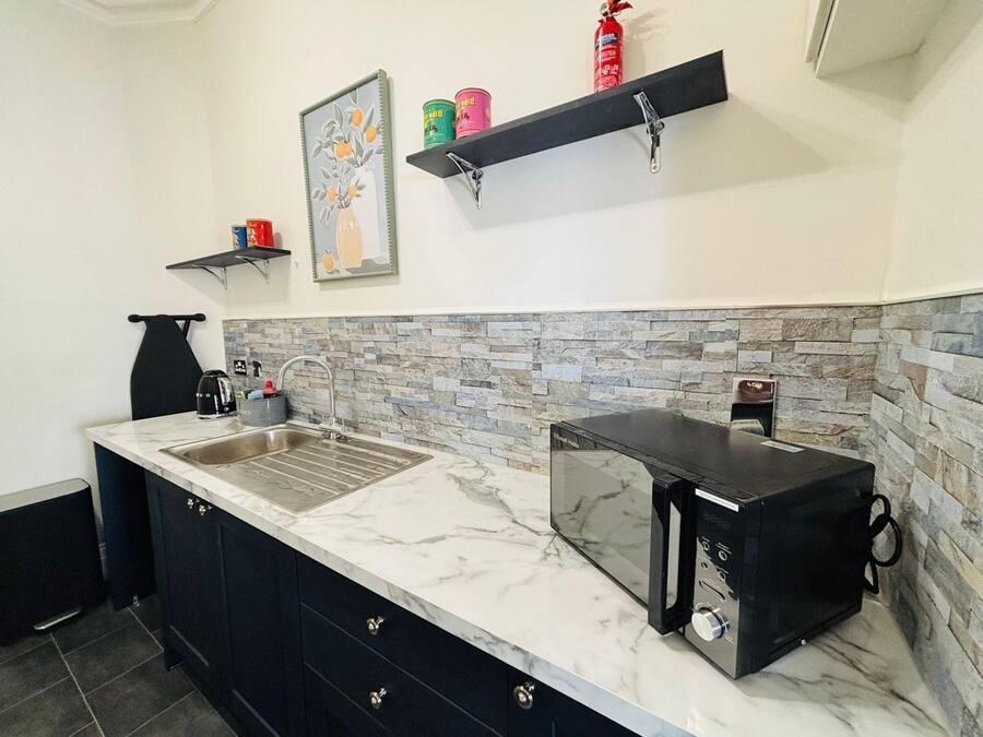 A kitchen with a marble countertop, black cabinets, a stone backsplash, a microwave, and a fire extinguisher on the wall.