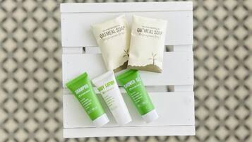 Un banco blanco con tres productos para el cuidado de la piel: dos tubos de champú y loción corporal verdes, y dos jabones de avena.