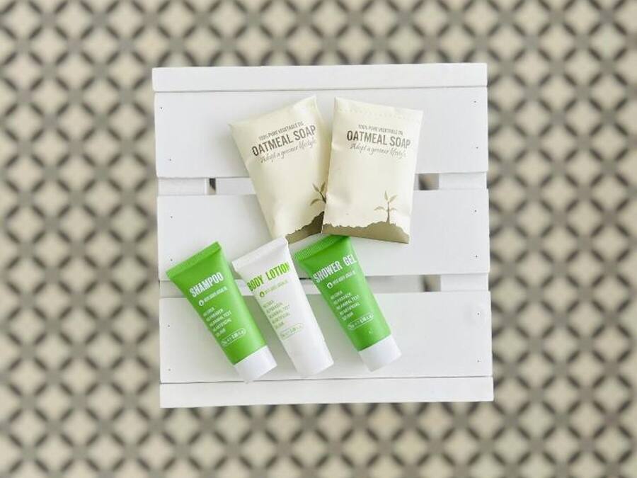Un banco blanco con tres productos para el cuidado de la piel: dos tubos de champú y loción corporal verdes, y dos jabones de avena.