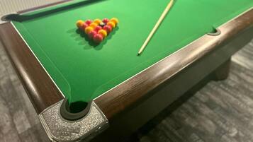 A pool table with a green felt surface, a cue stick, and a set of colored balls.