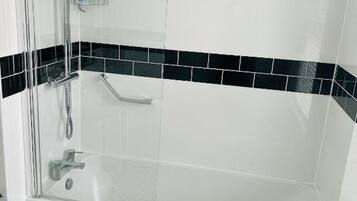 A glass-enclosed shower with a handheld showerhead and a handheld faucet.