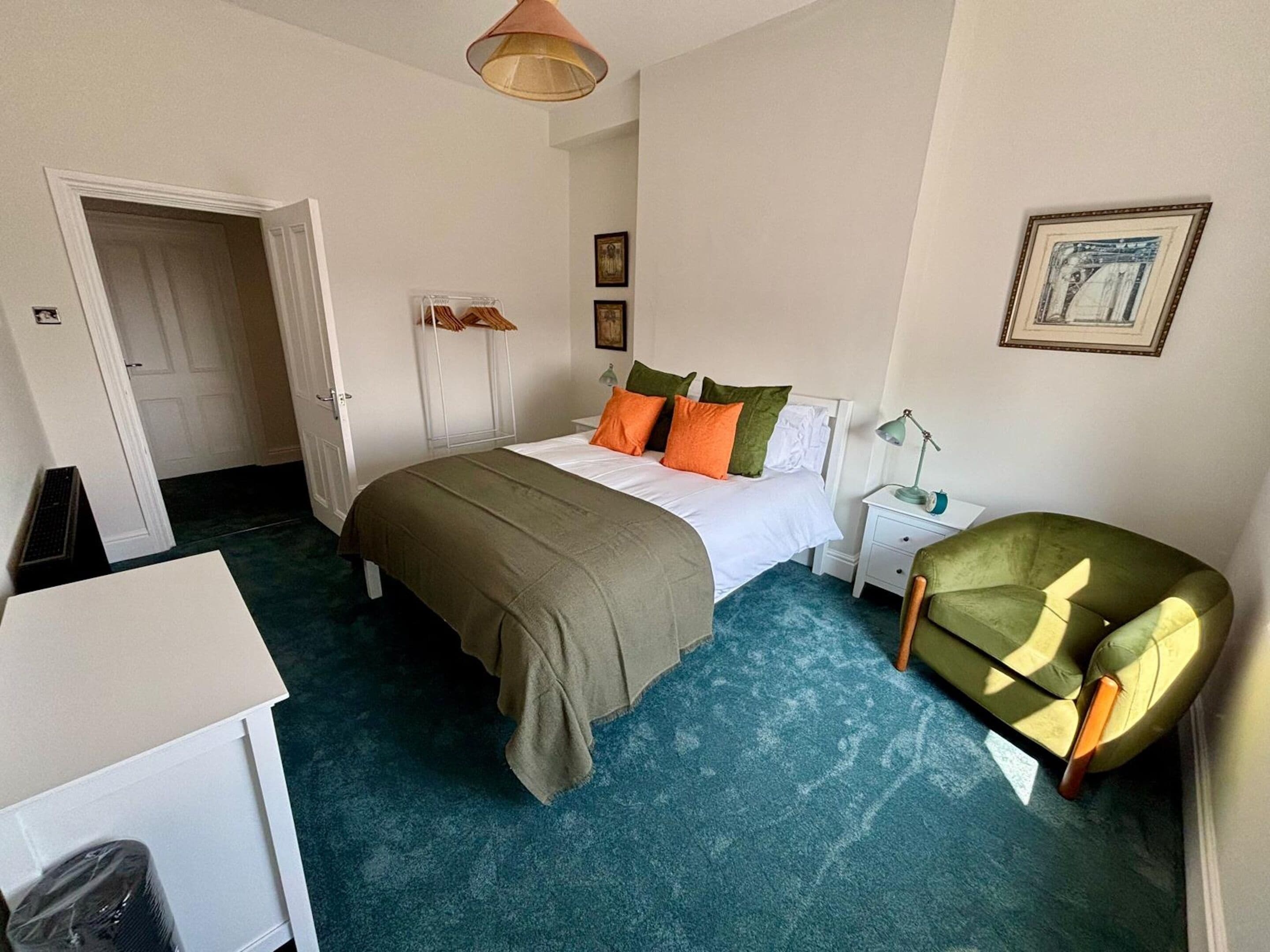 Une chambre à coucher comprenant un lit, une table de chevet, une lampe, une chaise et une porte donnant sur une autre pièce.