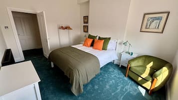 Une chambre à coucher comprenant un lit, une table de chevet, une lampe, une chaise et une porte donnant sur une autre pièce.