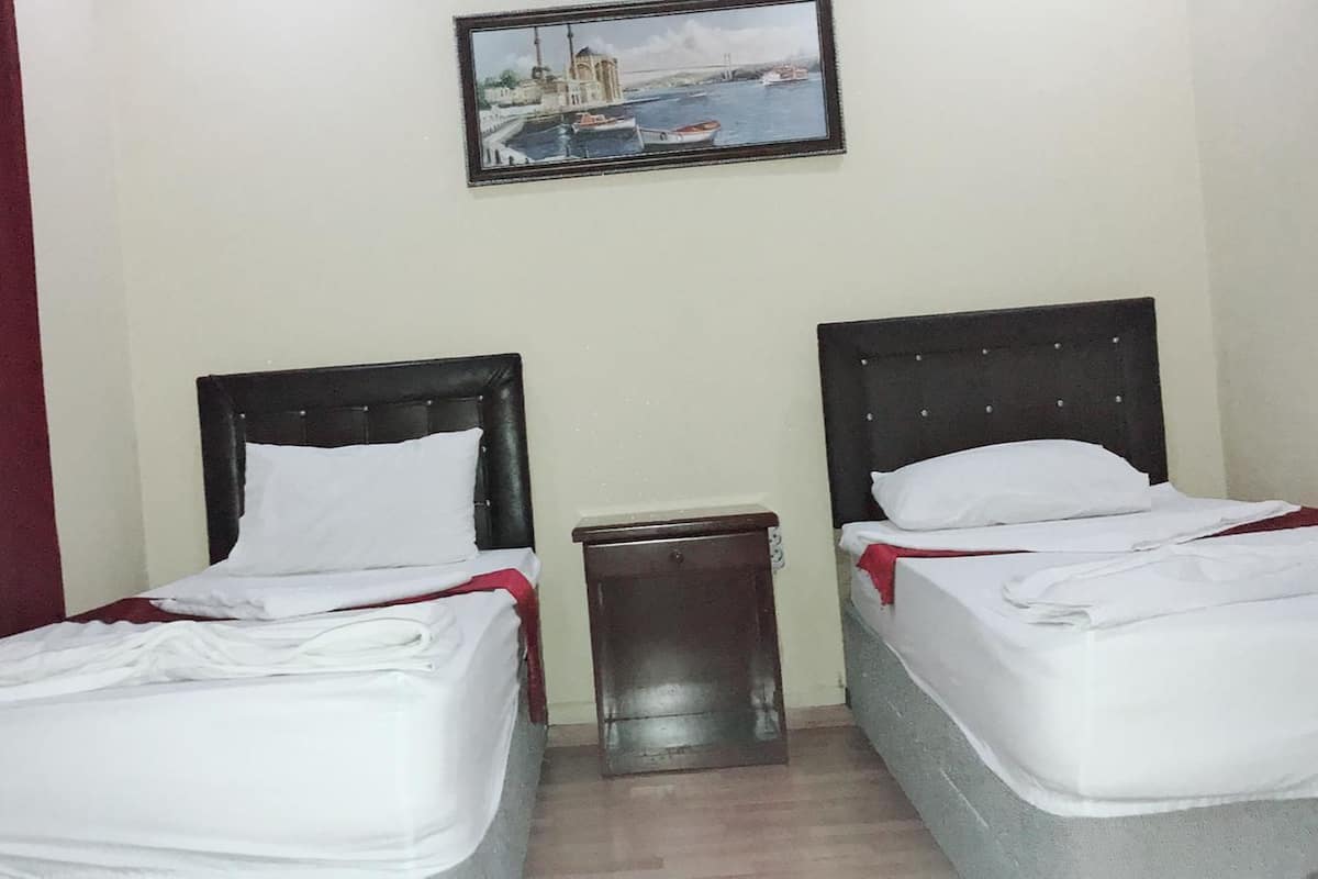 A hotel room with two beds, a small trash bin, and a painting of a bridge and boats on the wall.