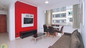 Un salon moderne avec un mur d’accent rouge, un téléviseur à écran plat, une table basse en verre, un canapé marron et un coin repas avec des chaises et une table.