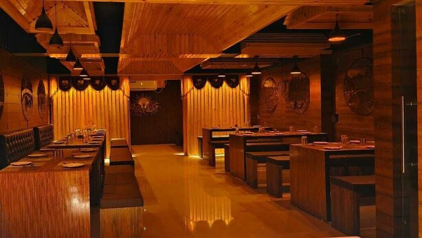 A restaurant with wooden walls and ceiling, long tables, and booths. - Hotel Blue Mmarlin (Port Blair)