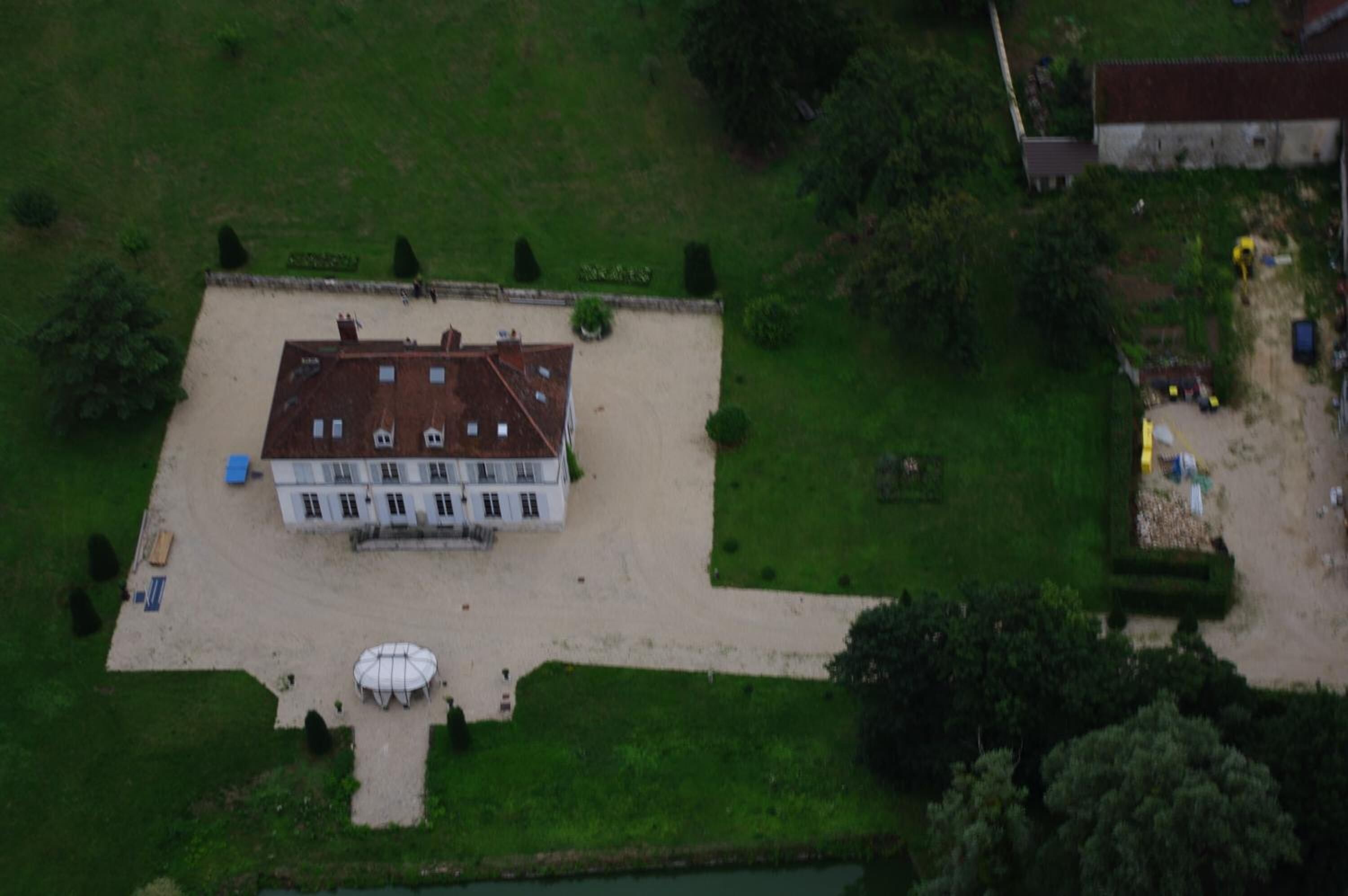 An aerial view of a large, rectangular building with a symmetrical facade, a central entrance, and a surrounding lawn.