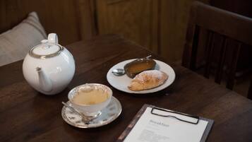 Un desayuno con tetera, un croissant y un tazón de sopa sobre una mesa de madera.
