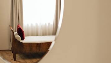 Un espejo redondo que refleja una esquina de una habitación con una silla de madera y un cojín rojo.
