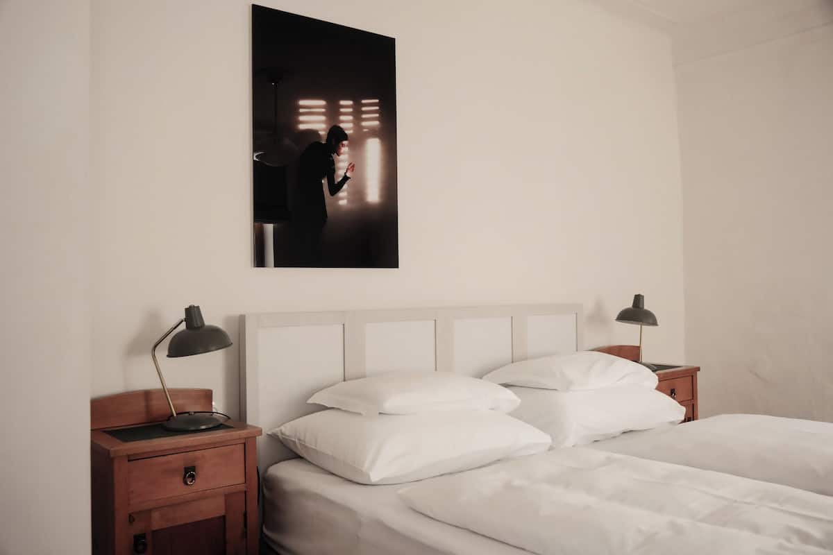 A bedroom with a bed, two bedside tables, a nightstand, a wall-mounted picture, and a ceiling light fixture.