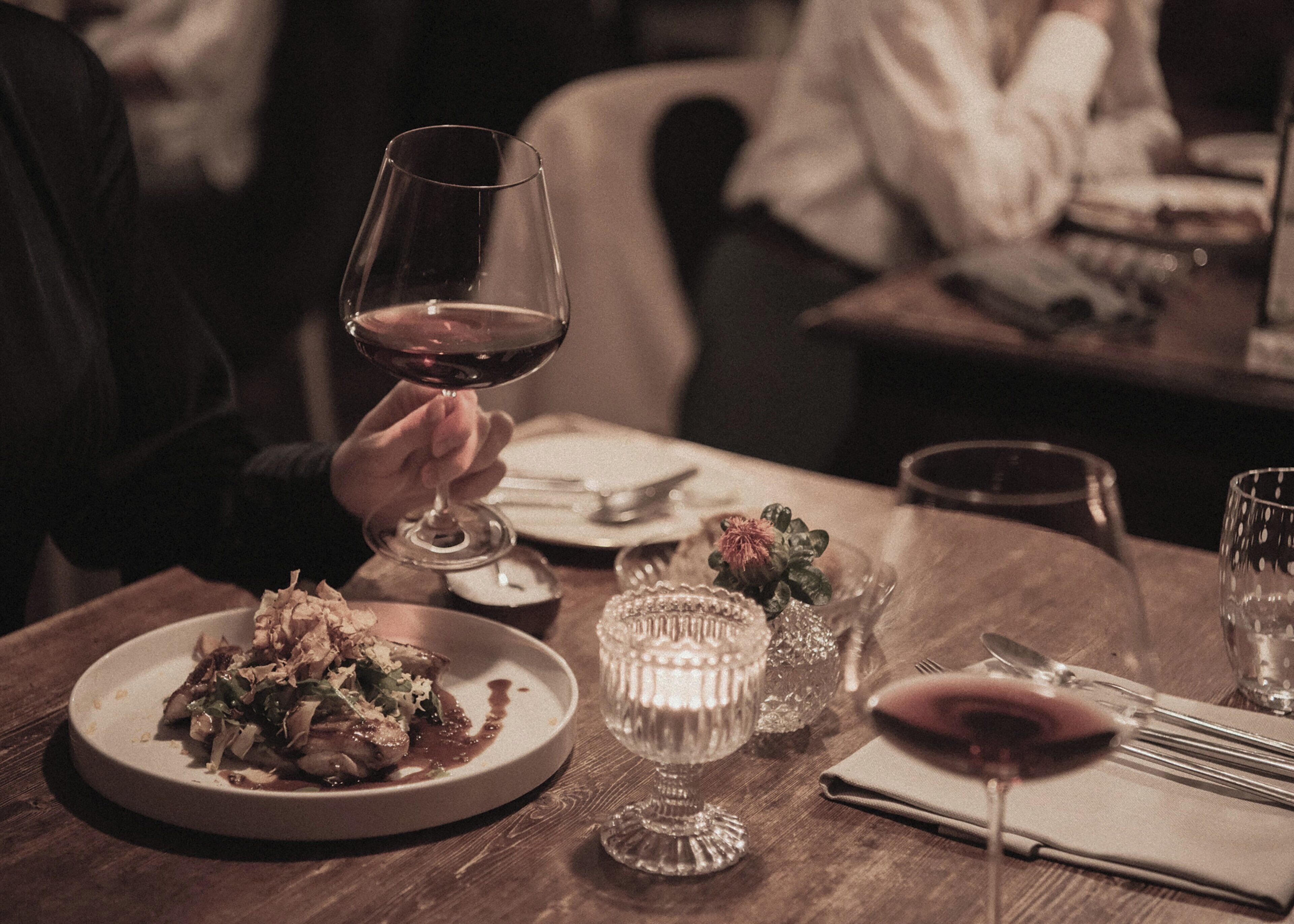 A dining table with a plate of food, a wine glass, and a candle.