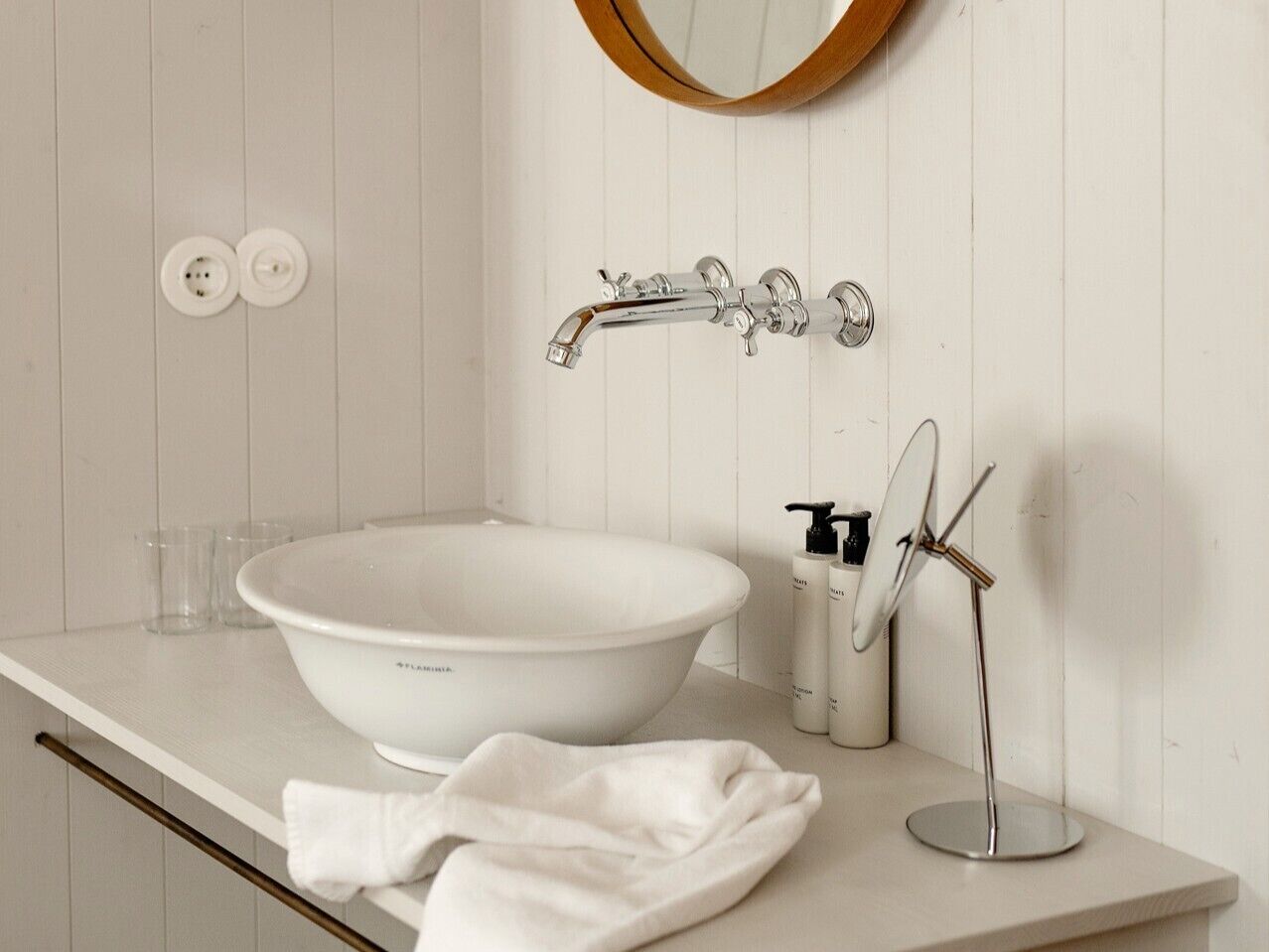 A bathroom with a white vessel sink, a round mirror, a handheld showerhead, and a towel on the counter.