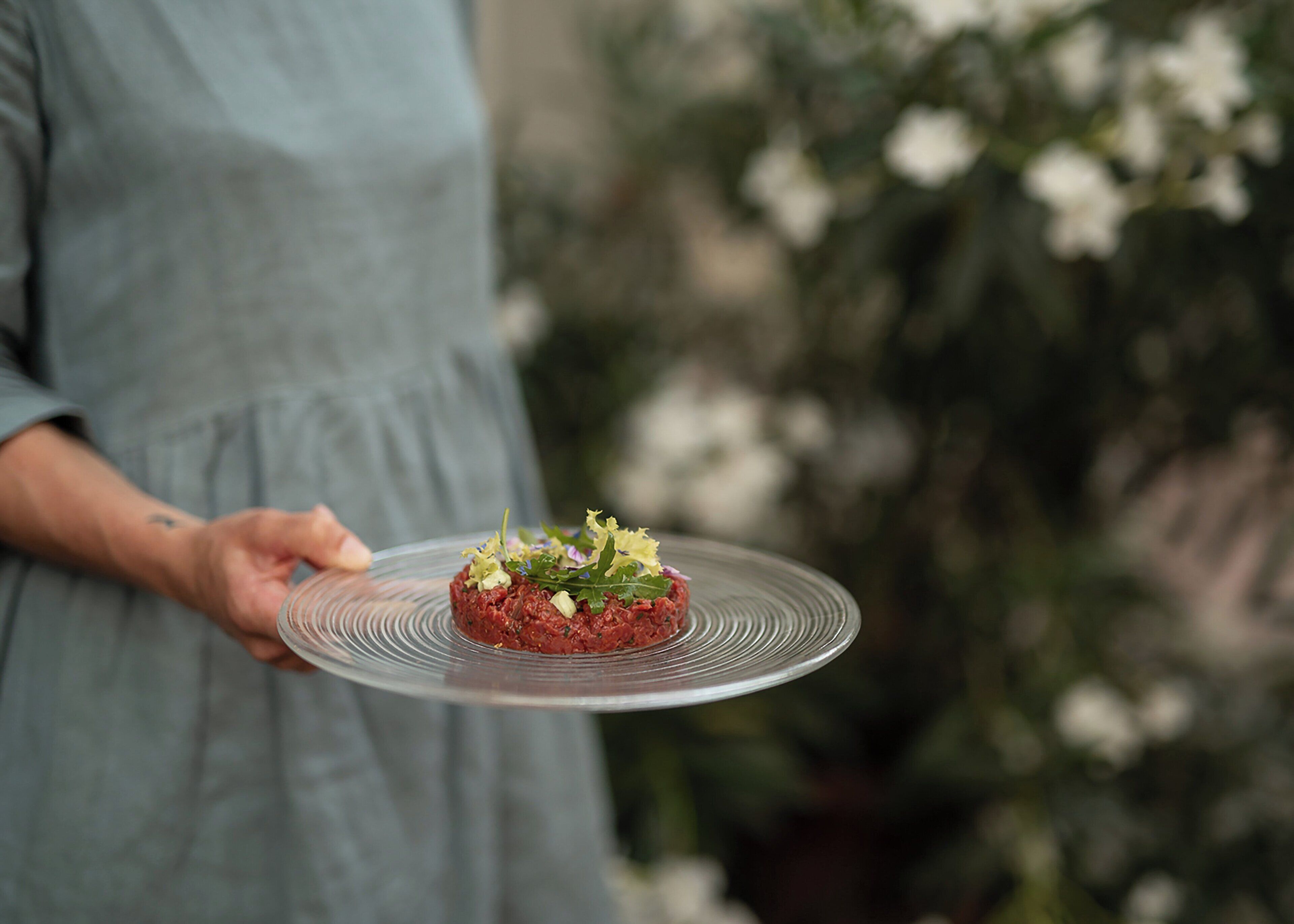 Una persona sosteniendo un plato transparente con comida cubierta de hojas verdes y hierbas.