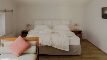 Un dormitorio con cama, mesitas de noche, una silla y suelo de madera.