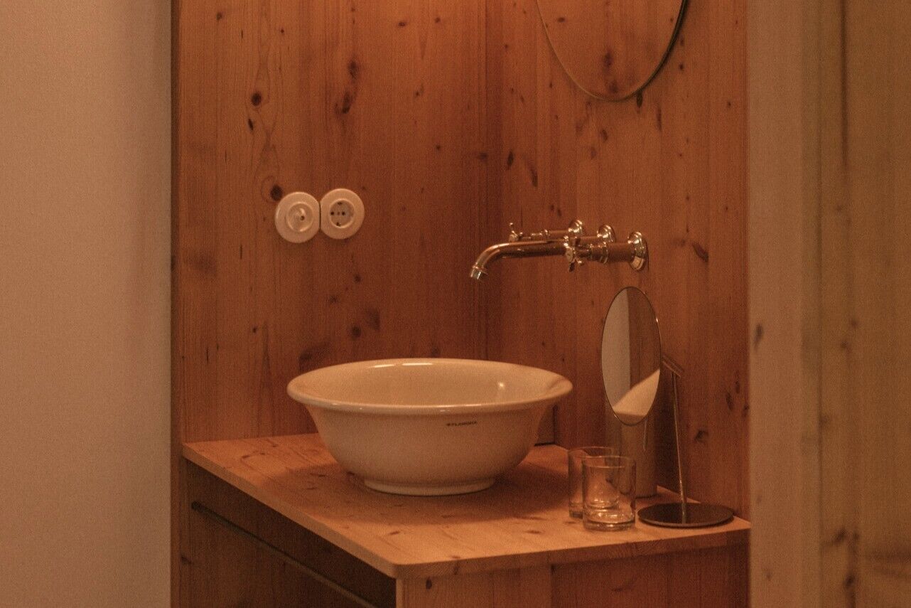 Un baño de madera con un lavamanos blanco, un espejo y un vaso.