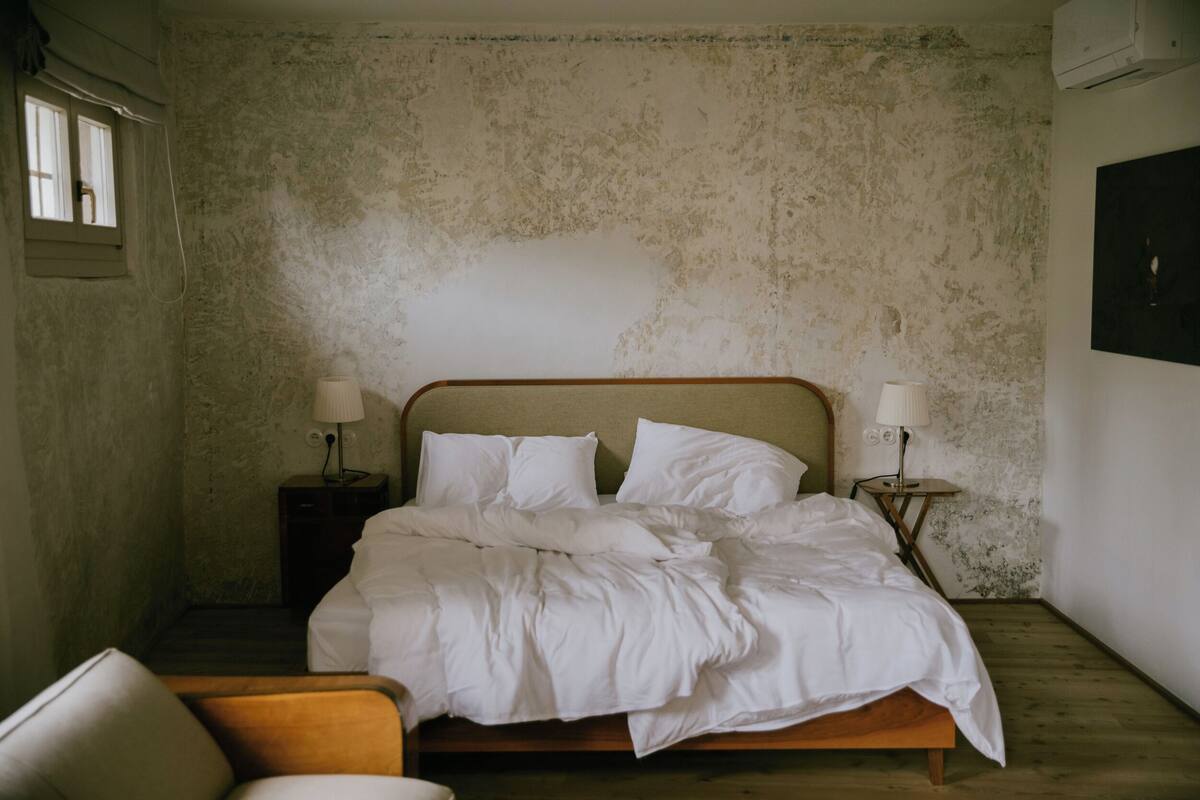 A bedroom with a wooden bed, two bedside tables with lamps, a chair, and a window.
