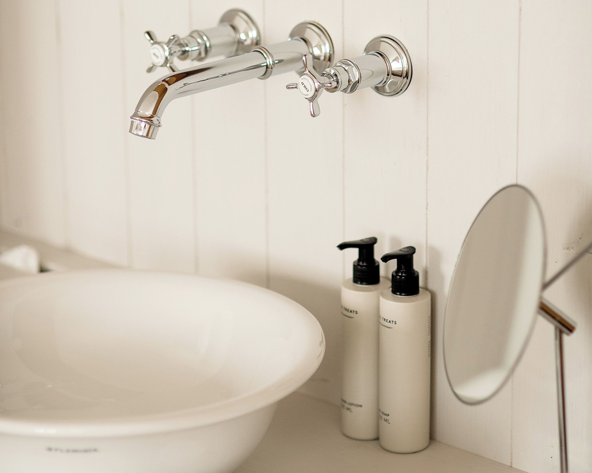 Un baño con un lavamanos blanco, dos botellas de loción y un espejo.