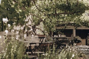 An outdoor dining area with wooden tables and chairs, surrounded by lush greenery and trees. - 1477 Reichhalter (Lana)