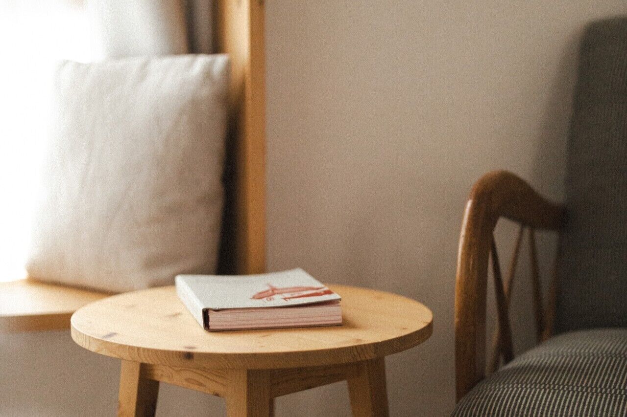 A round wooden table with a book and a cushion on it.