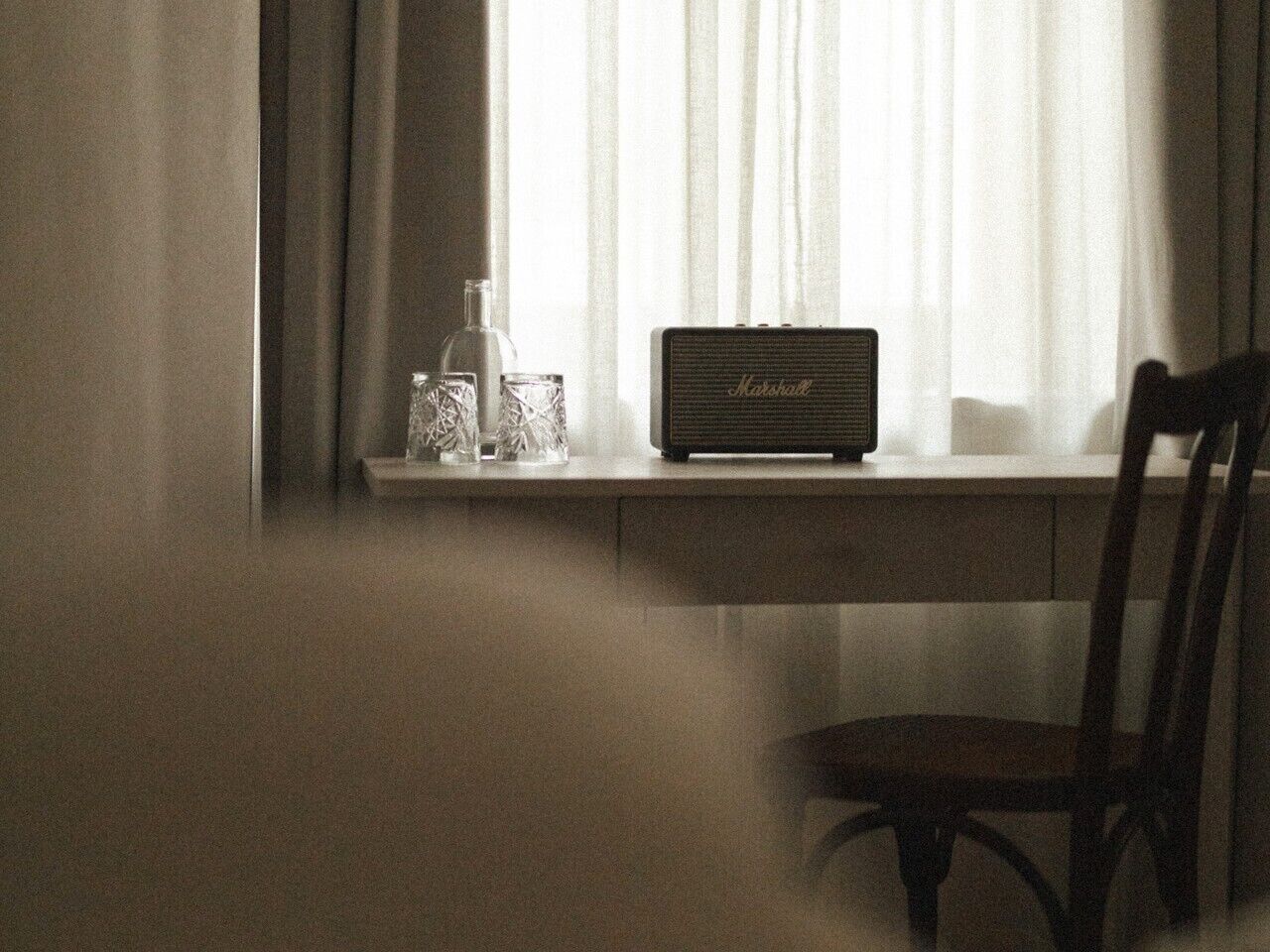 A vintage Marshall radio on a white desk by a window with sheer curtains.