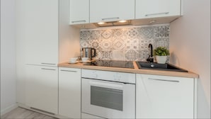 Una cocina moderna con armarios blancos, un salpicadero estampado, una cafetera y un lavamanos.