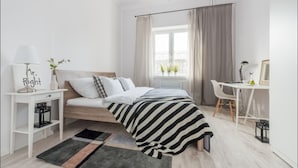 Un dormitorio moderno con cama, mesitas de noche, un escritorio y una ventana con cortinas.