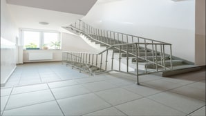 Una escalera moderna con barandillas de metal, piso de baldosas y vista a una ventana con plantas.