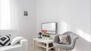 Una sala moderna con un sofá blanco, un sillón a cuadros de galgo, una mesa de centro con plantas y un cartel con una vista urbana enmarcada.