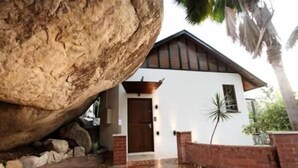 Ein Haus mit einem großen Felsen davor, einer weißen Fassade und einer braunen Tür.