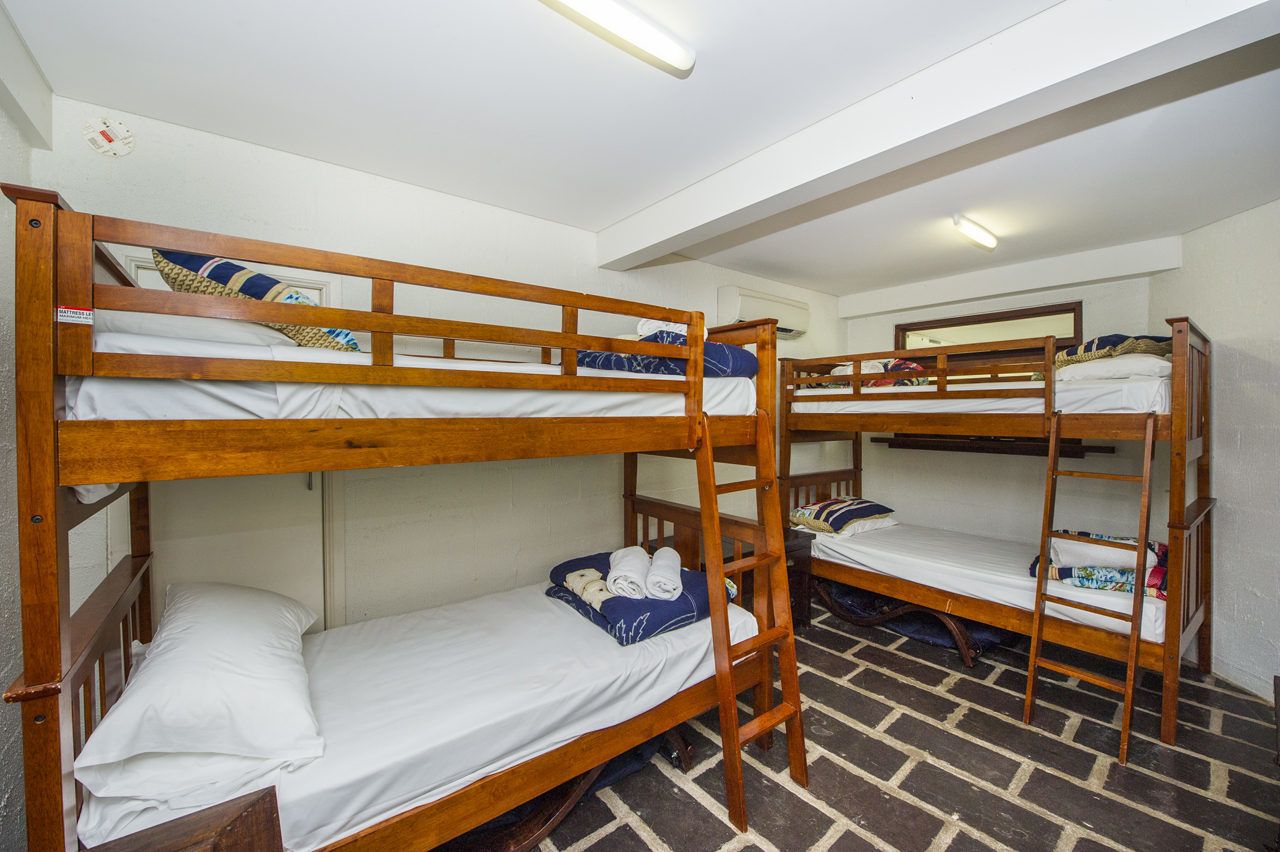Een slaapzaal met stapelbedden, een zichtbare airconditioning en een betegelde vloer.