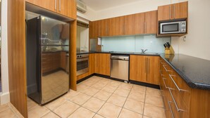 A modern kitchen with wooden cabinets, stainless steel appliances, and a black countertop. - Picnic Bay Apartments Unit 1 (Picnic Bay)