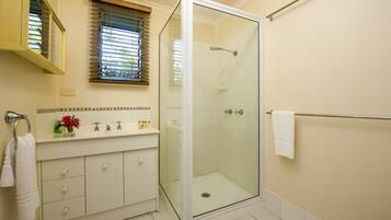 A bathroom with a glass-enclosed shower, a white vanity with a mirror, and a window with blinds.