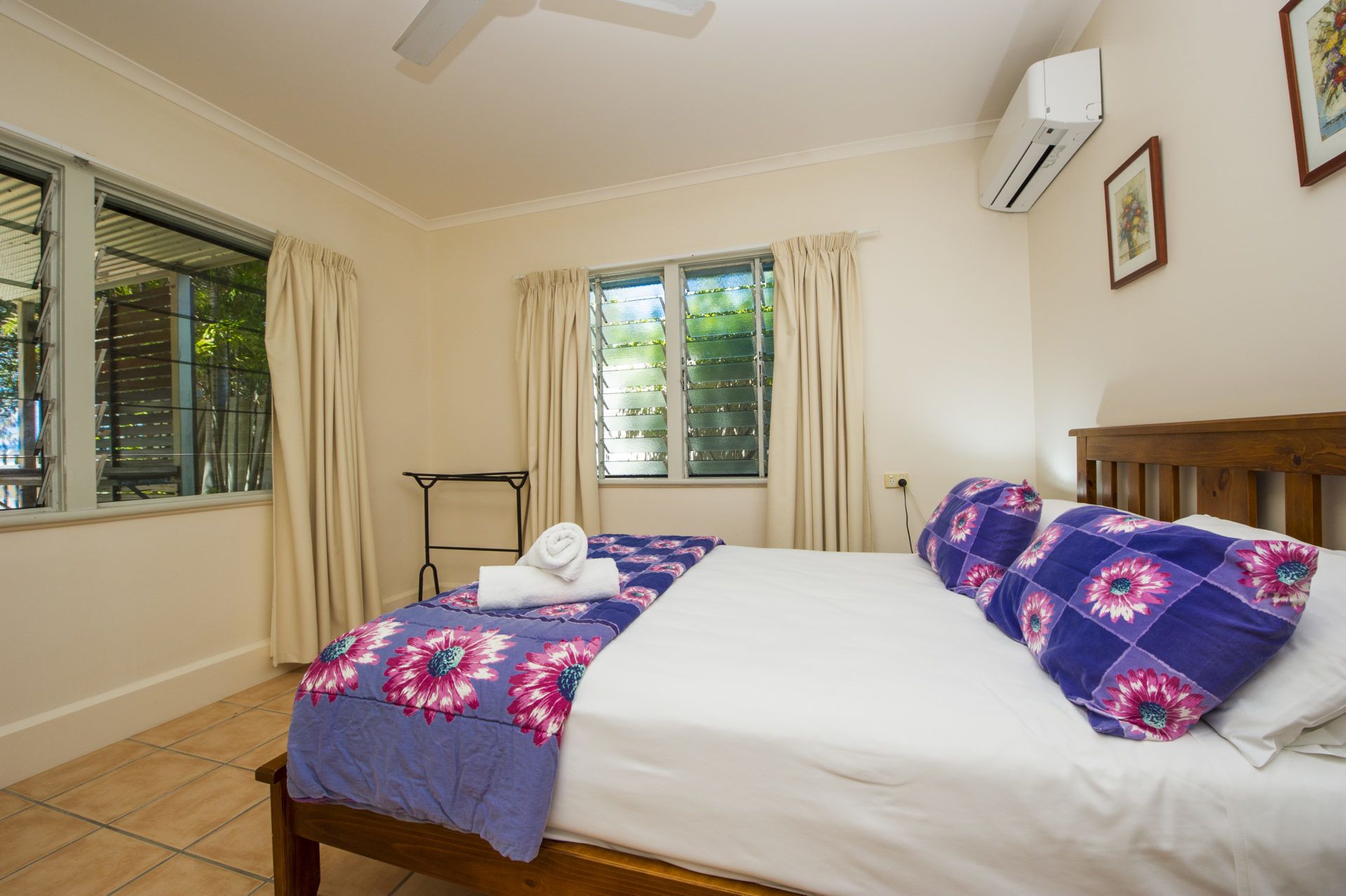 A bedroom with a bed, a window with curtains, an air conditioning unit, and a small table.