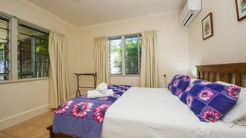 A bedroom with a bed, a window with curtains, an air conditioning unit, and a small table.