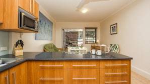 A modern kitchen with wooden cabinets, a built-in microwave, a granite countertop, and a ceiling fan. - Picnic Bay Apartments Unit 1 (Picnic Bay)