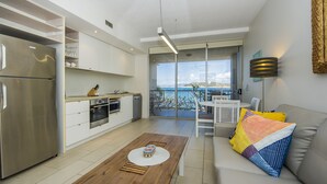 Una cocina moderna con un refrigerador de acero inoxidable, armarios blancos y una mesa de comedor de madera. Hay un balcón con vista al mar.