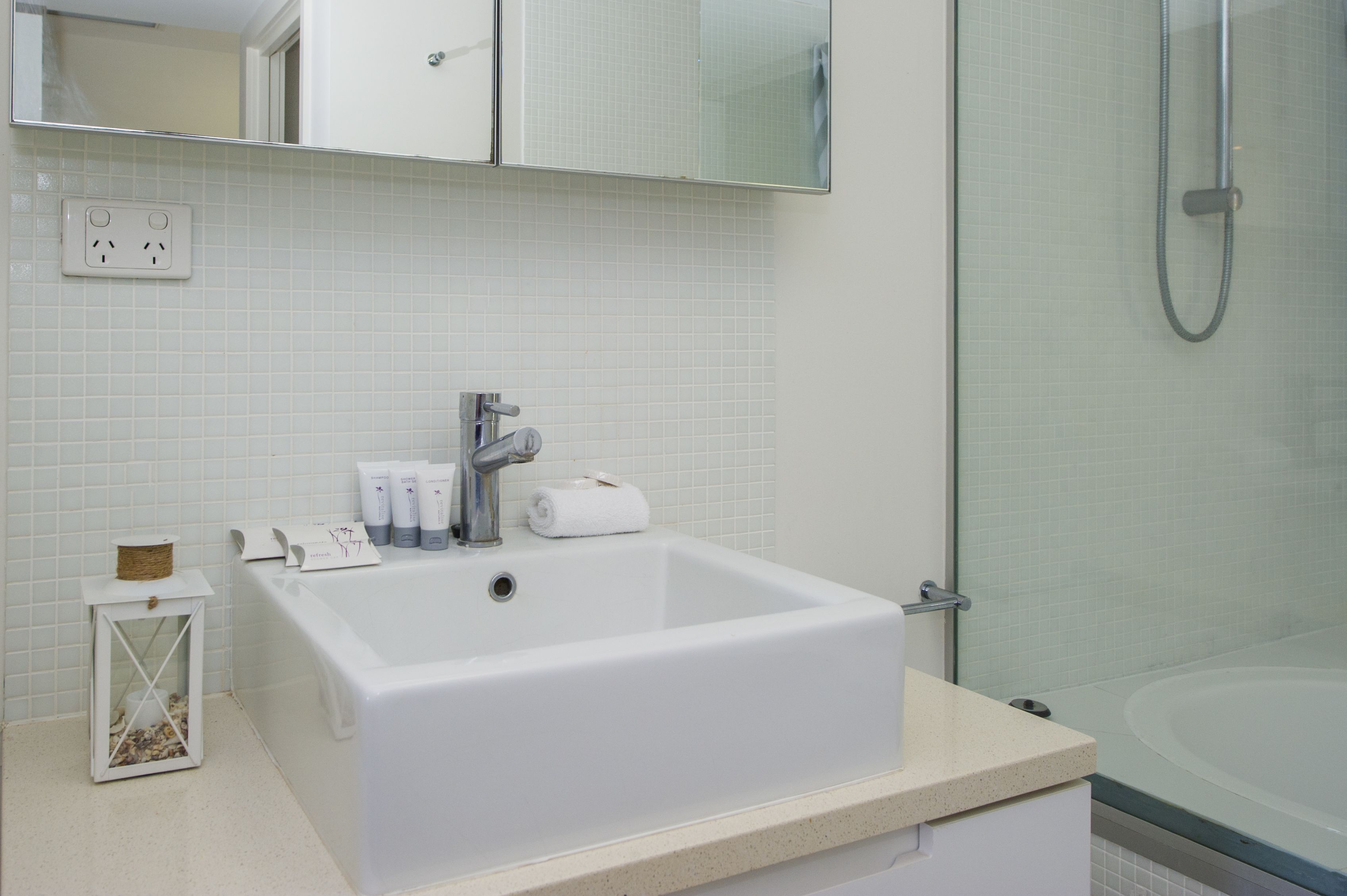 A bathroom with a white sink, a mirror above it, and a shower area.
